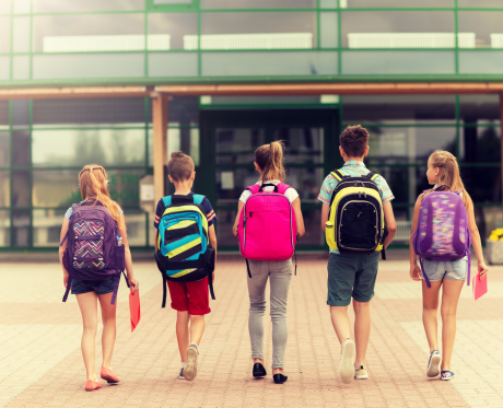 5 kids walking into school, each wearing a backpack
